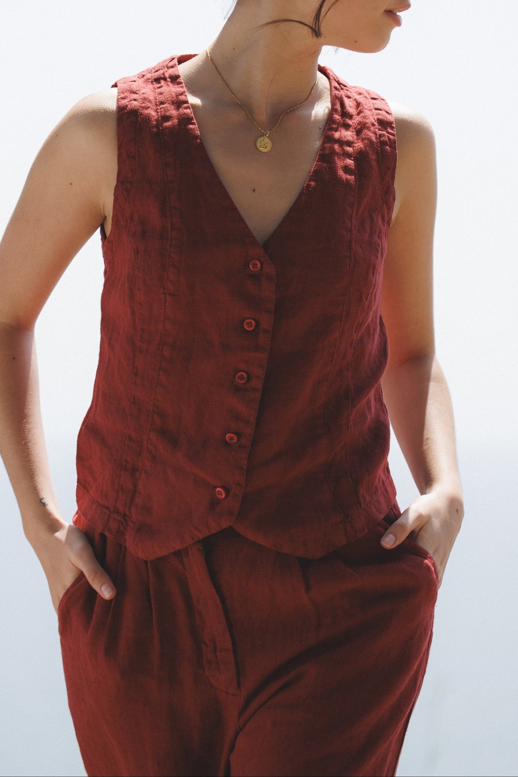 Female model,  wearing a dark red colored sustainable 100% linen vest with matching Italian handcrafted buttons paired with dark red linen trousers- VIR VITA
#color_sun dried tomato
