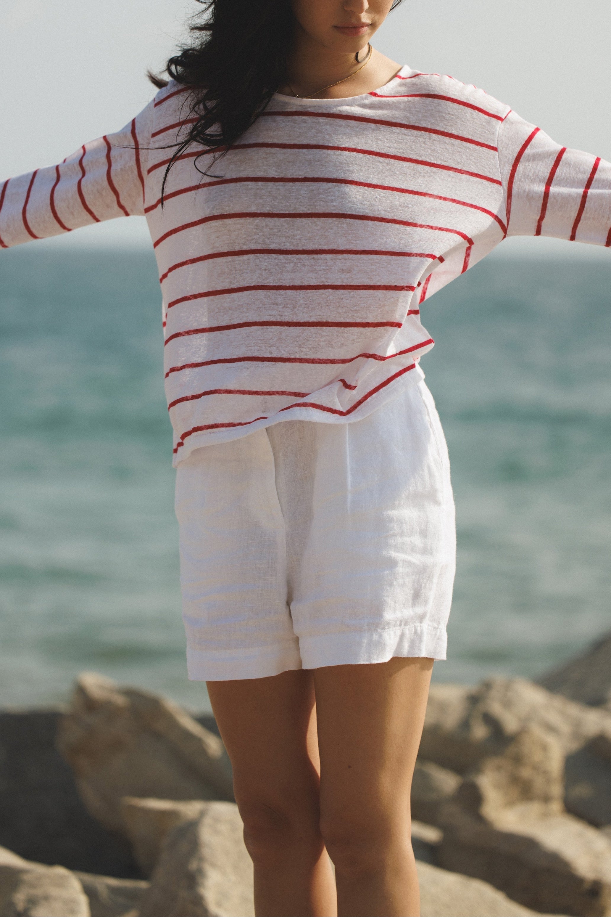 Female model wearing a 100% linen long sleeve striped top in white/red featuring a flattering scoop neckline and oversized fit at the beach- VIR VITA
#color_classic white/red