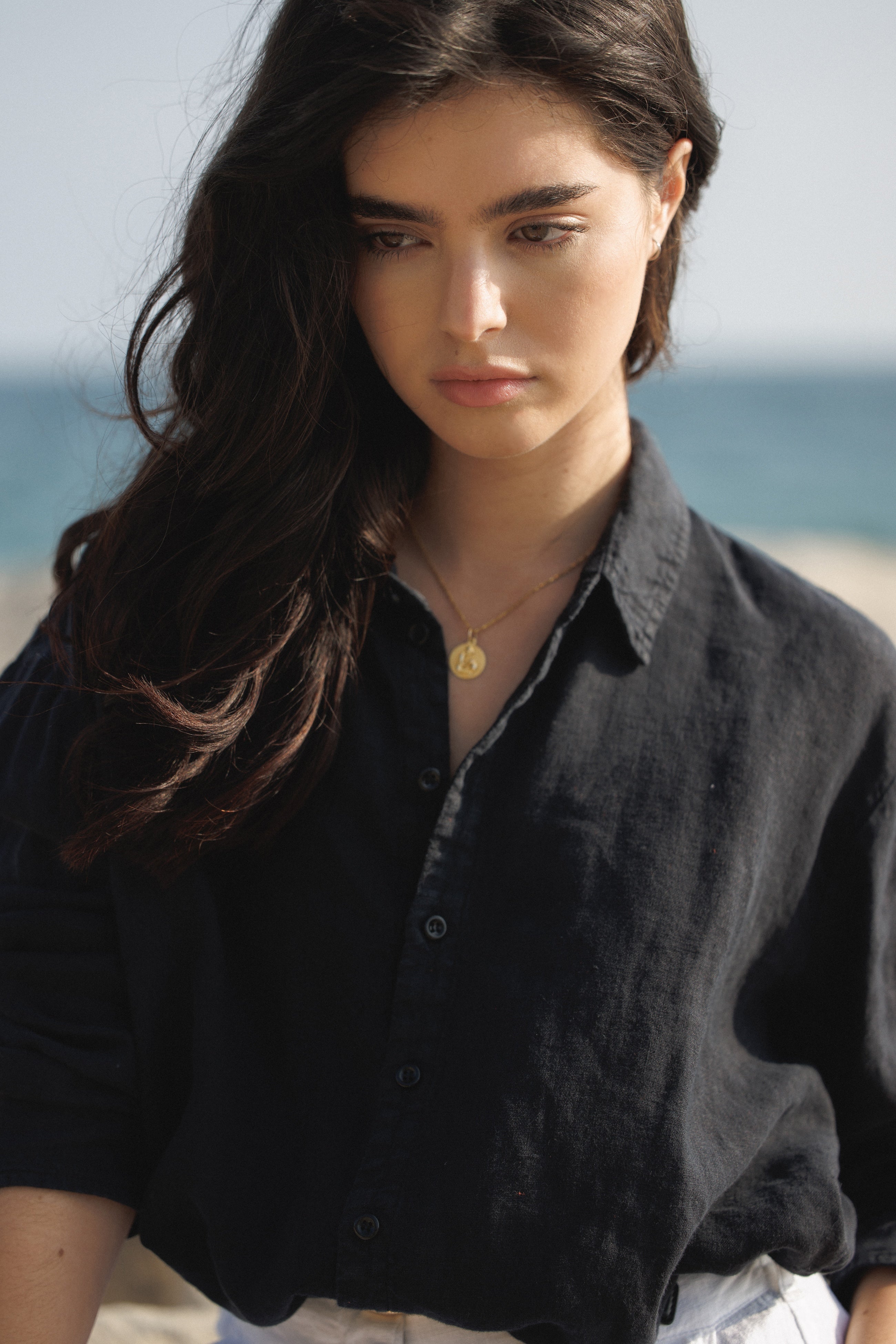 Female model,  wearing a black colored sustainable oversized linen button down long sleeve  with white linen trousers at the beach- VIR VITA
#color_black