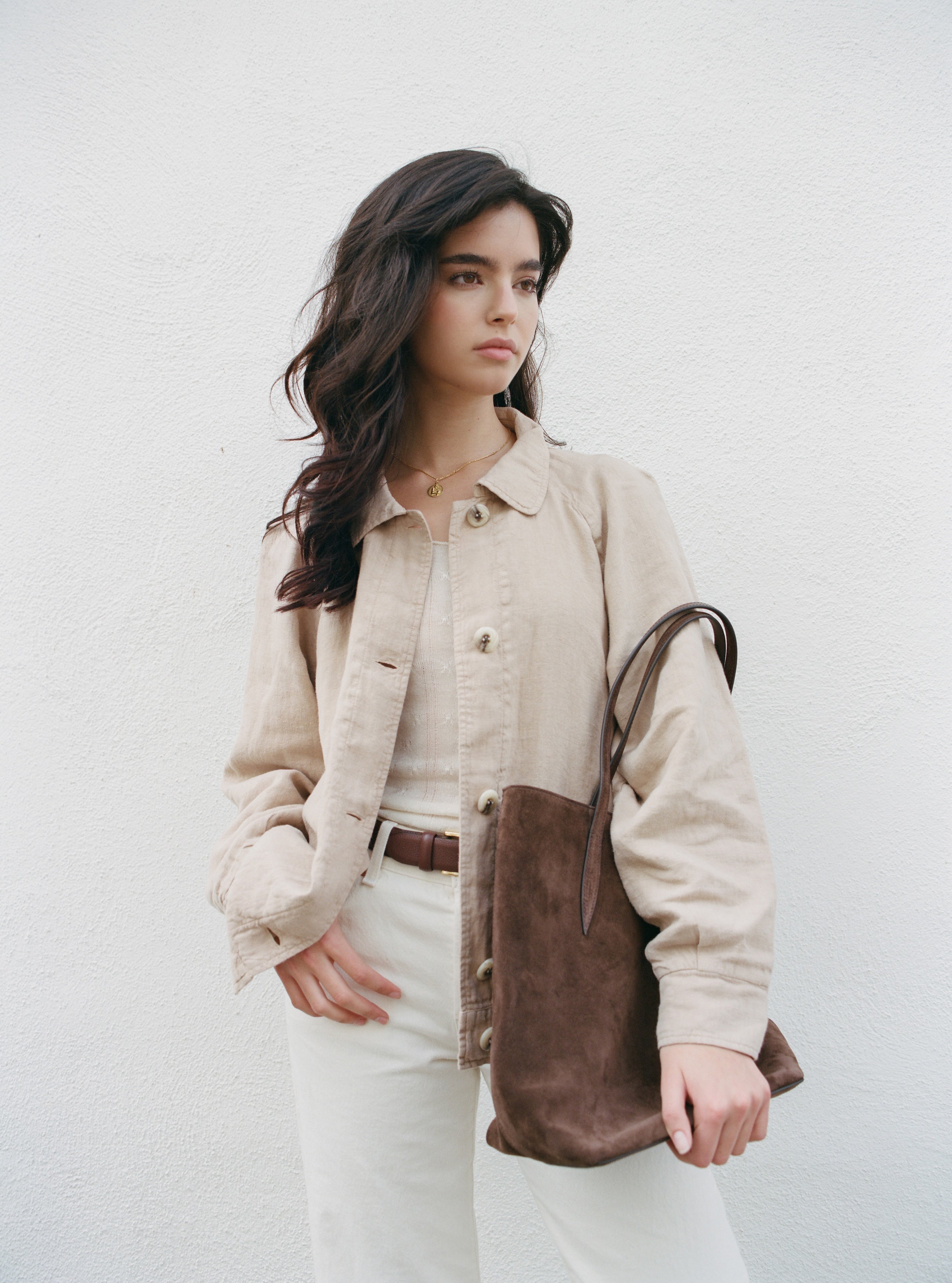 Female model wearing sustainable toffee beige linen barn jacket holding a brown suede bag -  VIR VITA 
#color_toffee