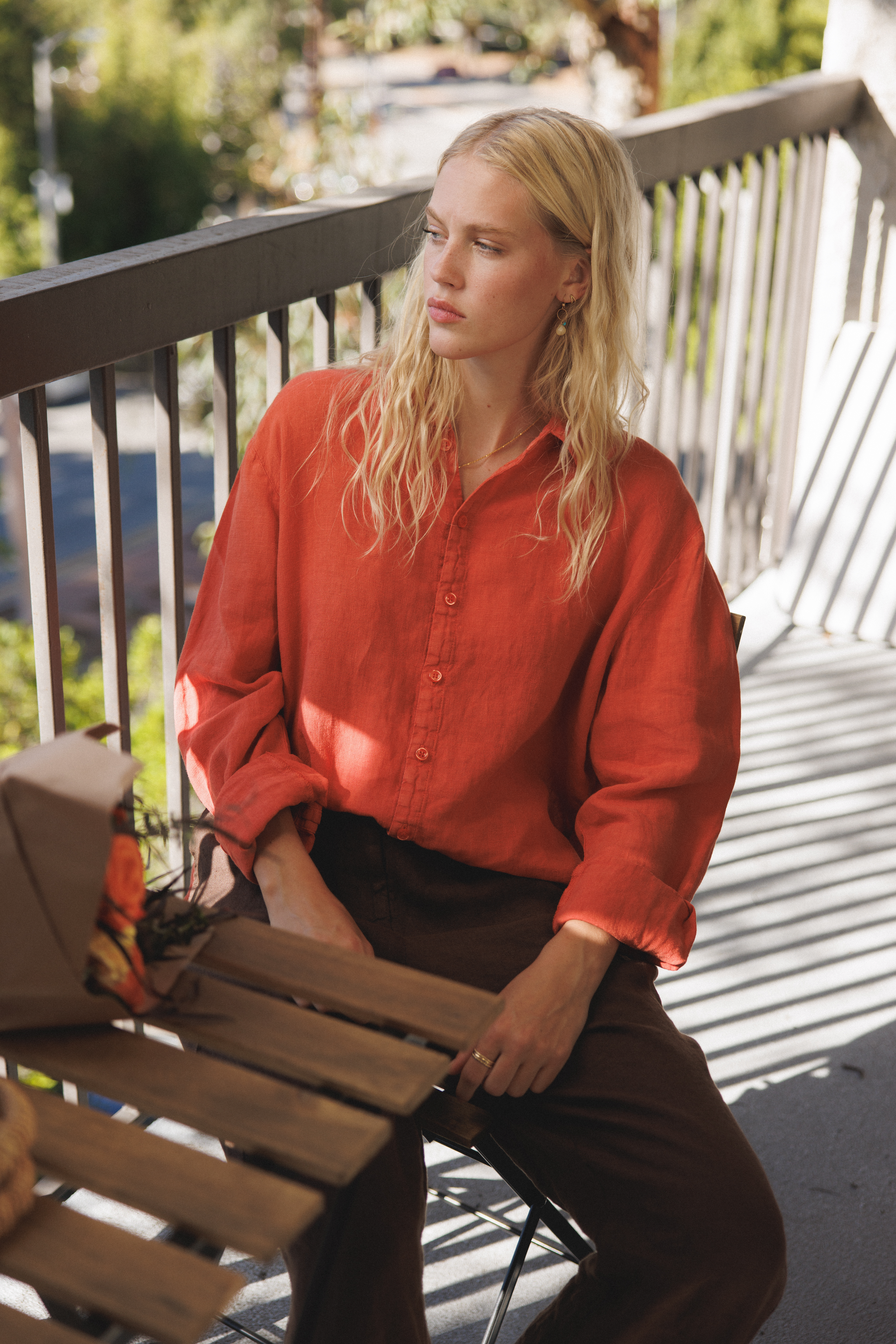 Female model, sitting on a balcony, wearing a cayenne / orange colored sustainable oversized linen button down long sleeve - VIR VITA
#color_cayenne