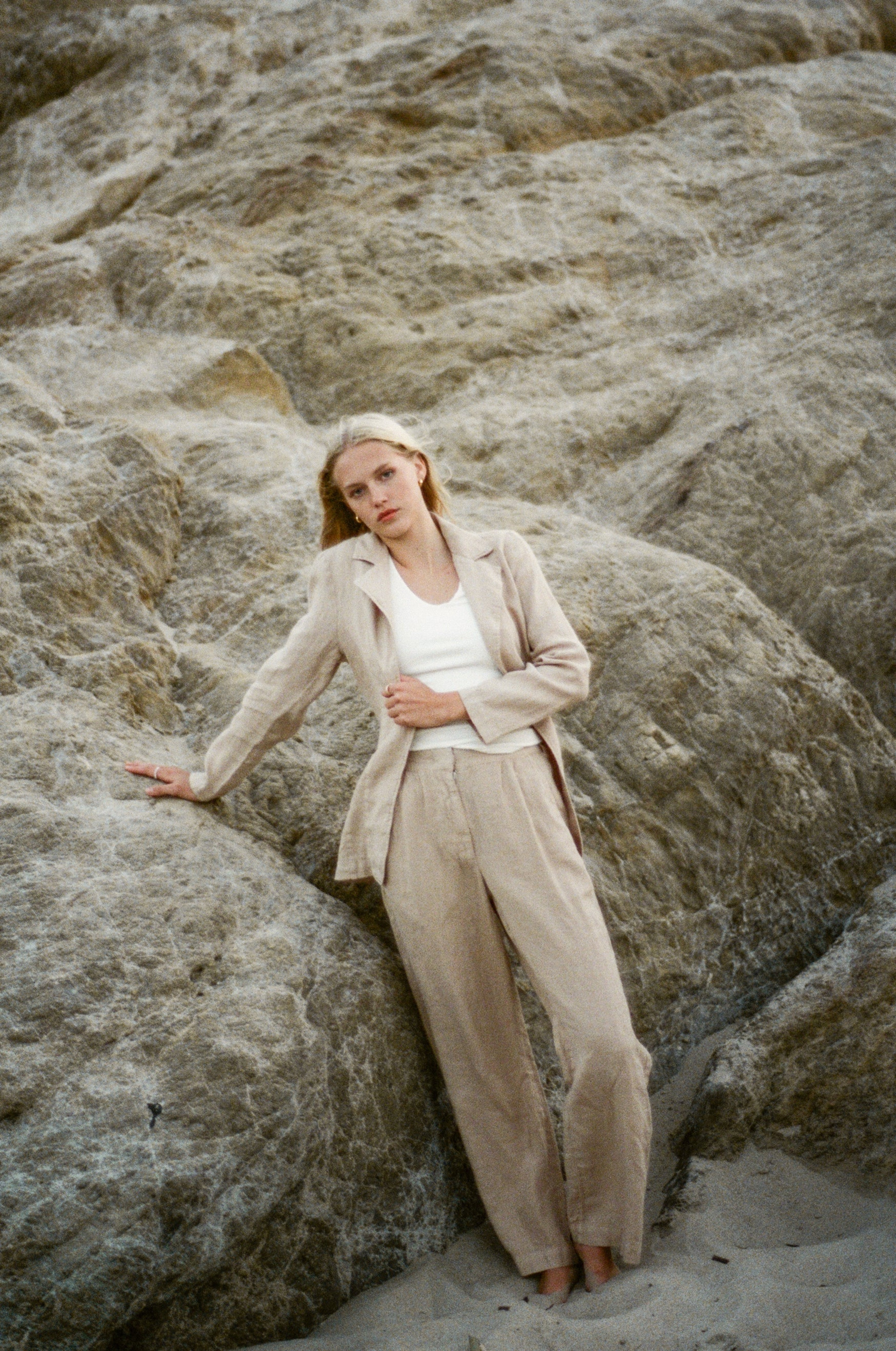 Female model wearing a 100% linen trouser featuring a high waisted double pleat silhouette in beige paired with a 100% linen blazer in beige on the beach- VIR VITA
#color_beige
