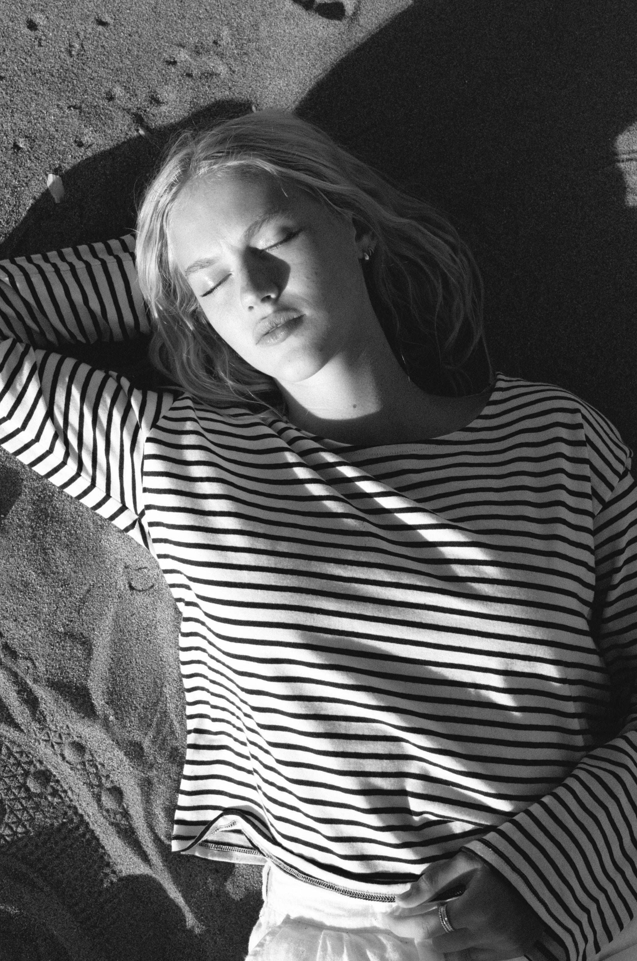 Female model, laying on the sand at the beach, wearing a sustainable long sleeve striped navy top - VIR VITA