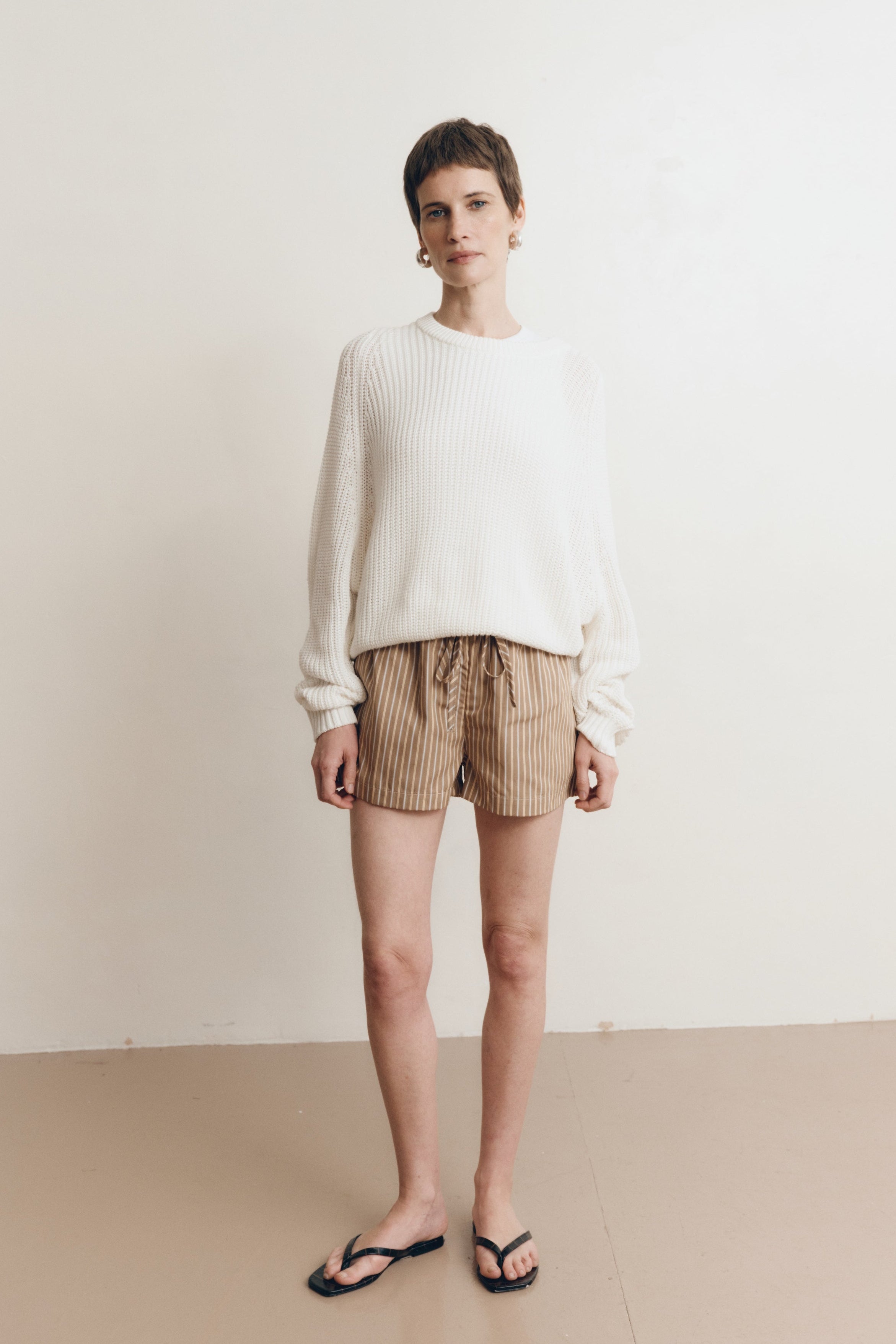 Posed female model wearing brown 100% cotton sustainable drawstring relaxed shorts paired with a cotton knit sweater in white and black sandals - VIR VITA
#color_canyon stripe