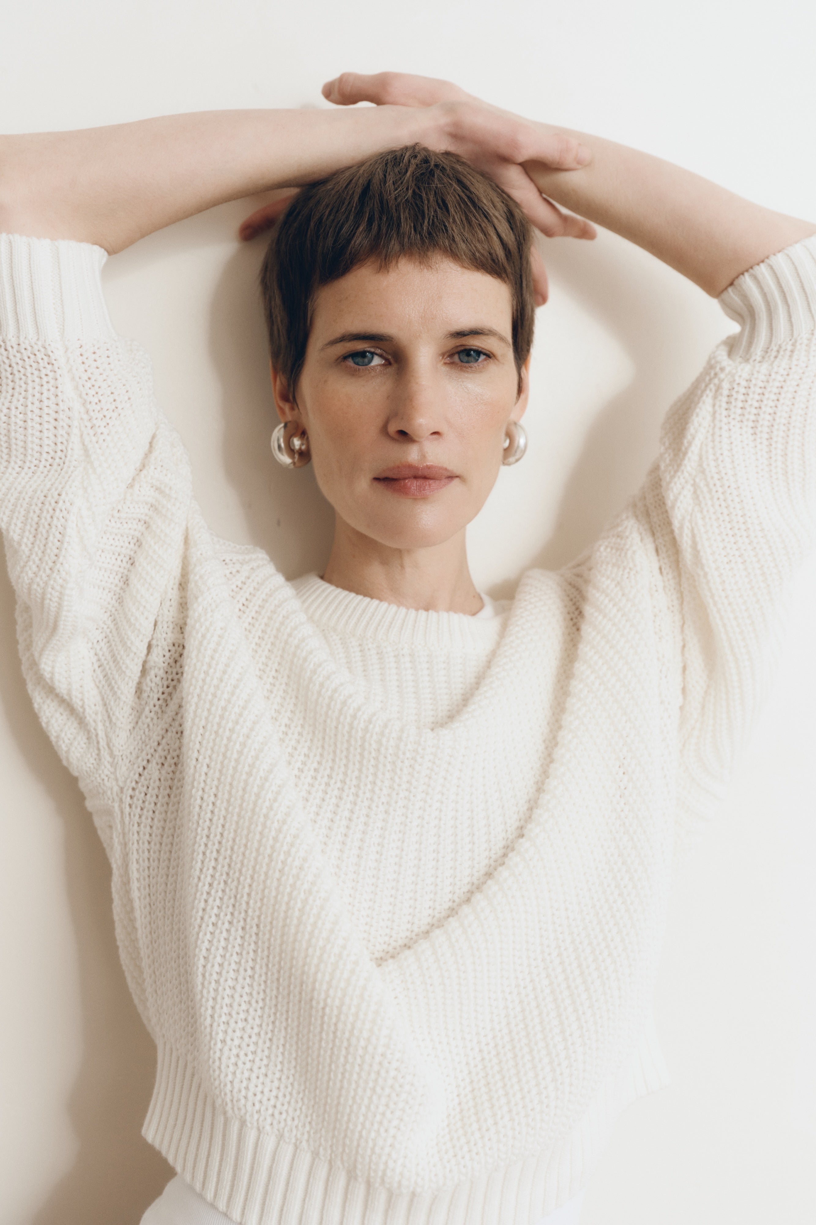Posed female model wearing a 100% cotton knit sweater with a flattering and subtly cropped silhouette in white - VIR VITA
#color_bone